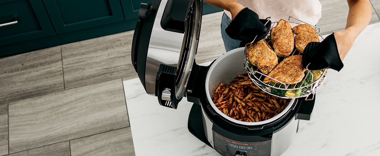 holding reversible roasting rack with chicken and broccoli over pressure cooker with pasta