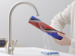 Person cleaning the brush bar of the Dyson 360 Vis Nav under a faucet