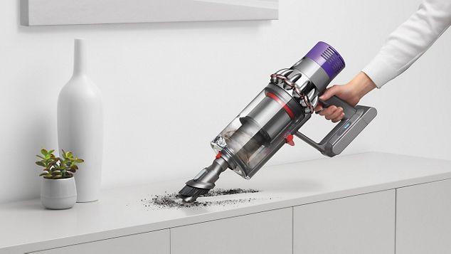 a hand holding Dyson V10 cleaning kitchen shelf