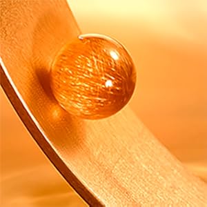 Extreme close-up of hair strand with amber colored protein bead on top of it.