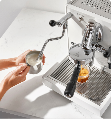 Person steaming milk and making espresso with a coffee machine.