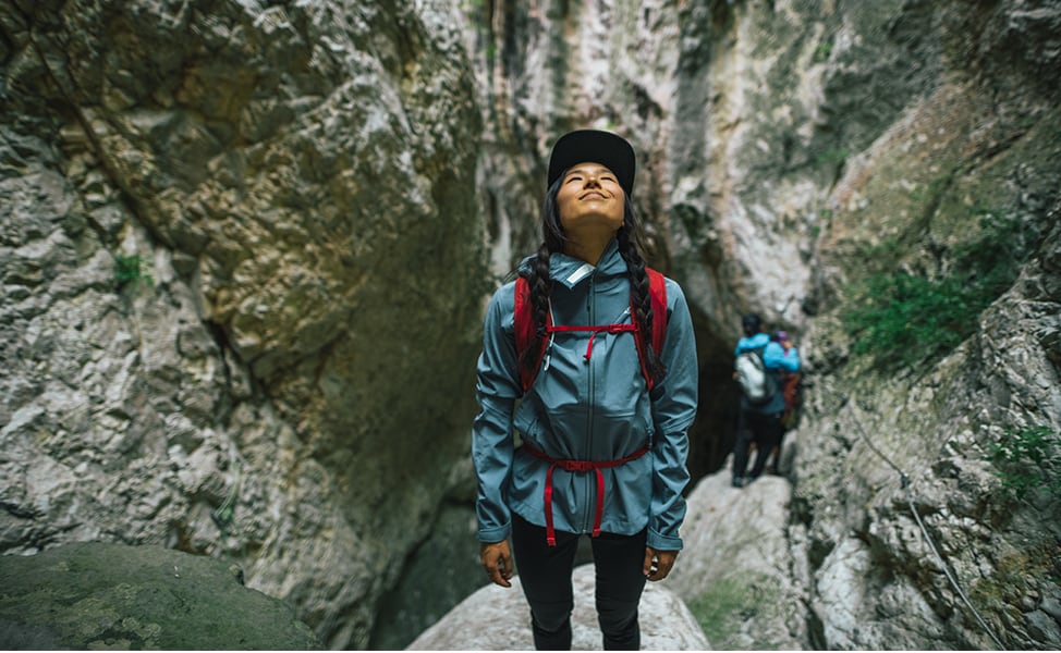 The woman stands on a rocky cliff and looks up at the sky.